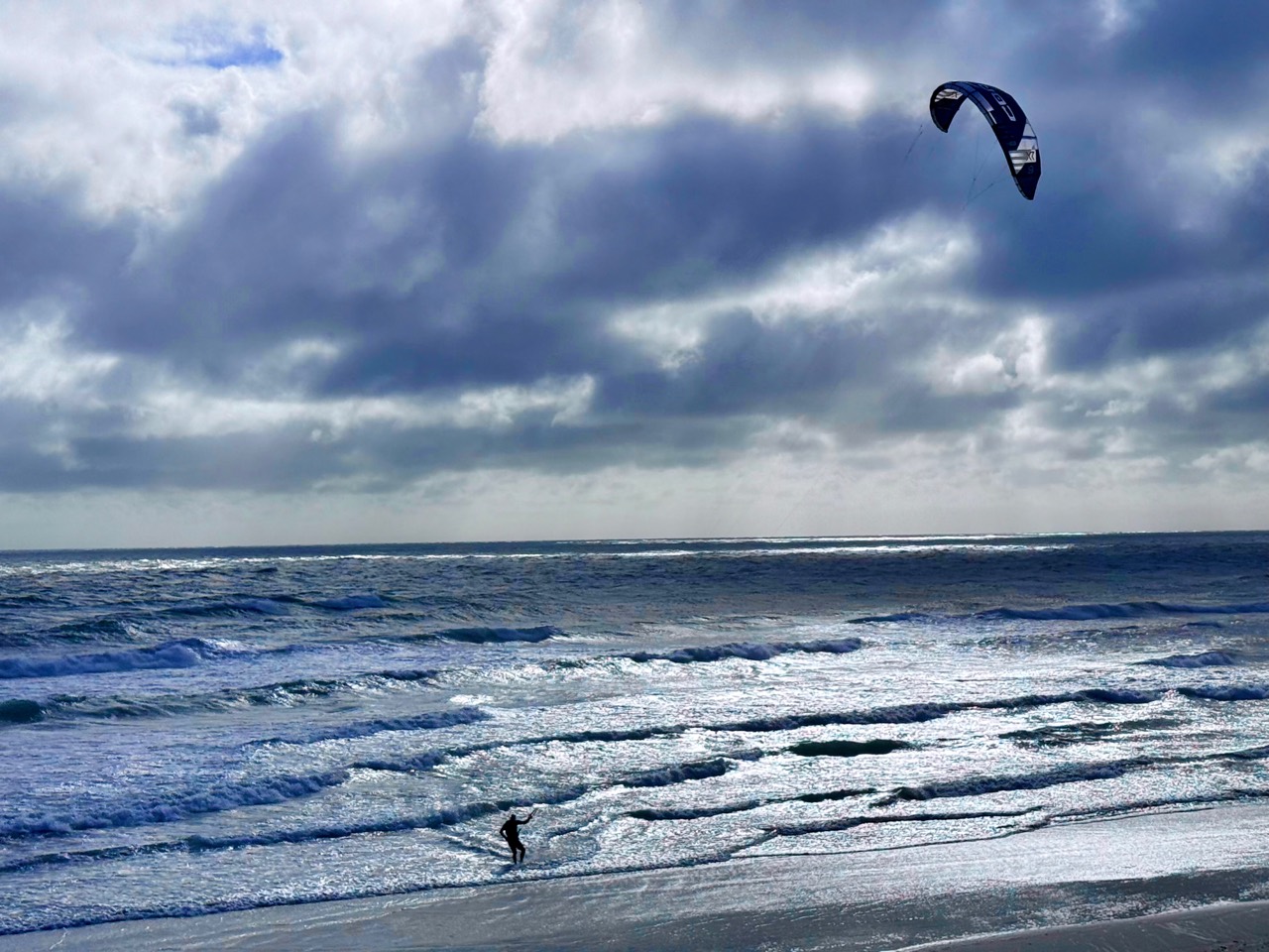 Ocean waves beneath dramatic clouds with a kite surfer at New Smyrna Beach